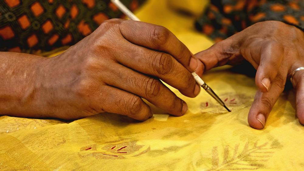 indische Kunsthandwerker malen auf Stoff auf einer Kunstreise durch Rajasthan